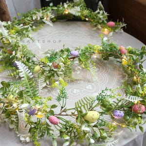 May include: A green and white garland with small pastel colored eggs and white fairy lights. The garland is perfect for Easter decorations.