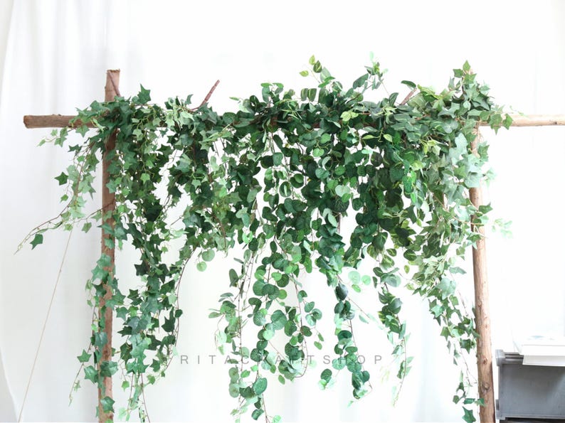 May include: Artificial green ivy garland hanging from a wooden archway. The garland is made of plastic leaves and vines and is perfect for adding a touch of greenery to any space.