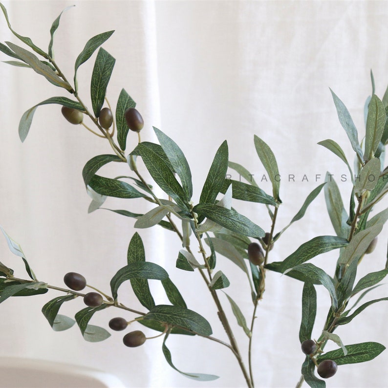 May include: A single artificial olive branch with green leaves and dark brown olives. The branch is perfect for adding a touch of nature to your home decor.