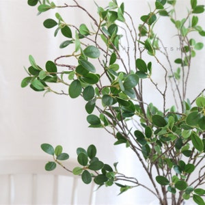 May include: A bunch of artificial green leaves on brown branches. The leaves are oval shaped and have a glossy finish. The branches are thin and have a natural look.