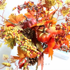 May include: An autumnal arrangement with miniature pumpkins, berries, and leaves in shades of orange, red, and yellow. The arrangement includes pinecones and a variety of berries. The overall theme is a celebration of the fall season.