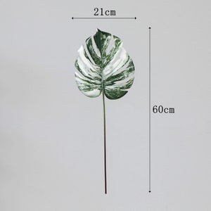 Op de afbeelding: Een enkel kunstmatig wit en groen monstera blad op een stengel, 21 cm breed en 60 cm hoog.