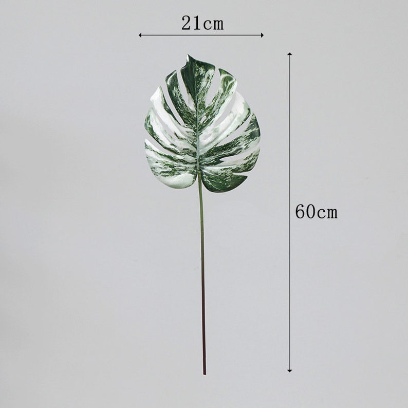 Op de afbeelding: Een enkel kunstmatig wit en groen monstera blad op een stengel, 21 cm breed en 60 cm hoog.