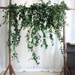 May include: Artificial green ivy garland hanging from a wooden frame. The garland is made of plastic leaves and vines. The garland is perfect for adding a touch of greenery to any space.