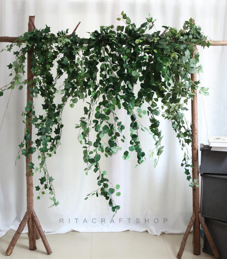 May include: Artificial green ivy garland hanging from a wooden frame. The garland is made of plastic leaves and vines. The garland is perfect for adding a touch of greenery to any space.