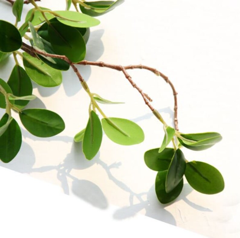 May include: A branch of artificial greenery with small, oval-shaped leaves. The leaves are a vibrant green color and the branch is brown.