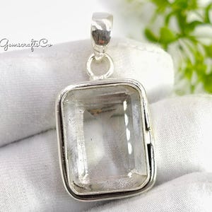 Op de afbeelding: Een rechthoekige hanger met een heldere, facetgeslepen edelsteen gezet in een zilverkleurig metalen frame. De hanger heeft een oogje voor een ketting en wordt gepresenteerd op een witte ondergrond. De tekst "Gemscrafts Co" is zichtbaar.