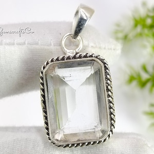 Könnte beinhalten: Ein rechteckiger, klarer Edelsteinanhänger mit einer silberfarbenen Öse. Der Edelstein ist facettiert und in einen silberfarbenen Rahmen mit einem gedrehten Seildesign gefasst. Der Anhänger wird auf einer weißen Oberfläche präsentiert. Der Text "Gemscrafts Co" ist sichtbar.