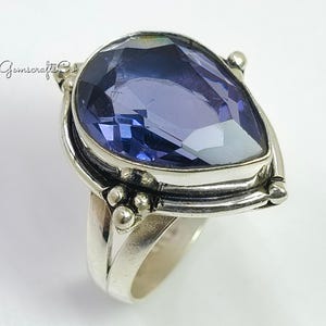 May include: A sterling silver ring featuring a large, pear-shaped, deep blue gemstone. The ring has a detailed setting with decorative silver accents. The gemstone is faceted, catching the light and creating a sparkling effect. The ring is set against a white background.