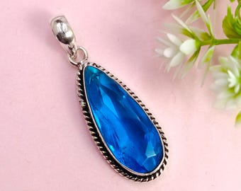 May include: A teardrop-shaped pendant with a large, faceted, bright blue gemstone. The gemstone is set in a silver-colored metal frame with a twisted rope design around the edge. The pendant has a silver bail at the top for a chain.