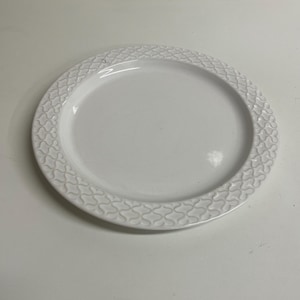 Può includere: Un piatto in ceramica bianca con un motivo decorativo in rilievo attorno al bordo.