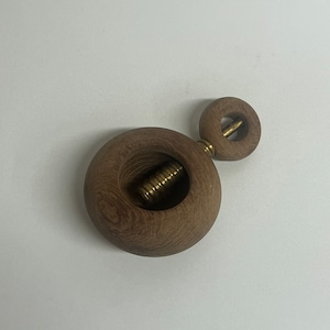 May include: A wooden nutcracker with a round, brown body and a smaller, round, brown top. The nutcracker has a brass screw in the center of the body.