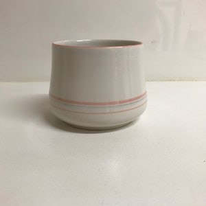 May include: A white ceramic cup with a pink and gray stripe design.