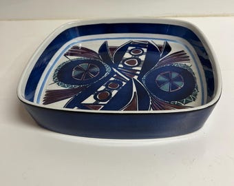May include: A square ceramic serving dish with a navy blue exterior and a white interior. The interior features a geometric design in shades of blue, burgundy, and white. The dish has rounded corners and a slightly raised edge.