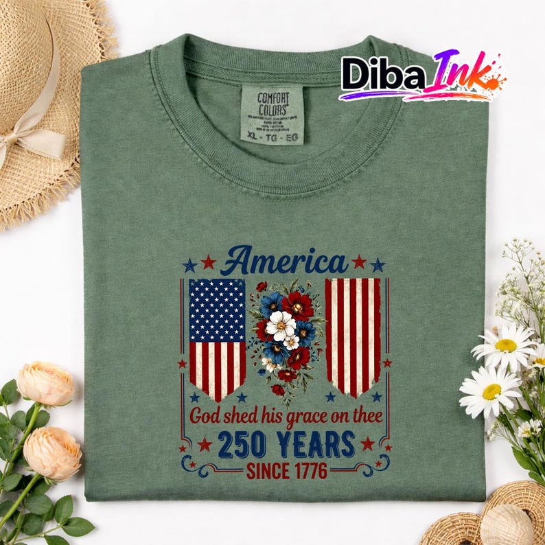 May include: Green Comfort Colors t-shirt with a patriotic design. The design features the word "America", a floral arrangement, and two American flags. The text "God shed his grace on thee" and "250 YEARS SINCE 1776" are also included.