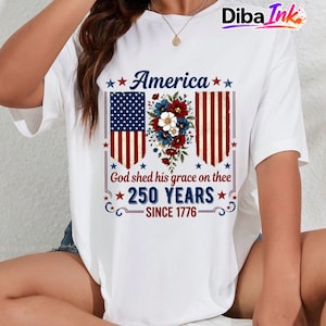 May include: White t-shirt with a patriotic design. The design features the word "America" above a floral arrangement and the American flag. Below the flag are the words "God shed his grace on thee" and "250 YEARS SINCE 1776."