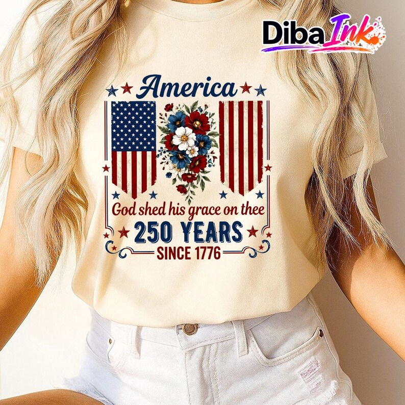 May include: A cream-coloured t-shirt with a patriotic design. The graphic features the American flag, floral elements, and the text: "America," "God shed his grace on thee," "250 YEARS," and "SINCE 1776."