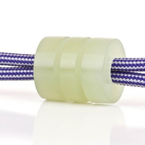 May include: A close-up of a white cord lock with a purple and white striped cord threaded through it.
