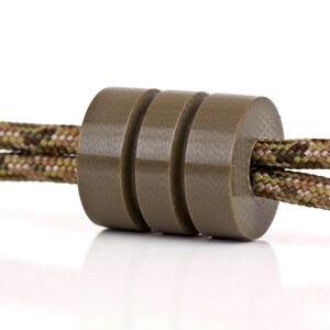 May include: A close-up of a brown cord lock with a camouflage pattern cord threaded through it.