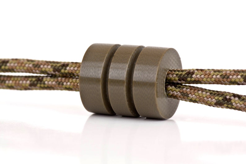 May include: A close-up of a brown cord lock with a camouflage pattern cord threaded through it.