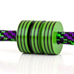 May include: Three green and black striped beads strung on a black and green rope with purple accents.