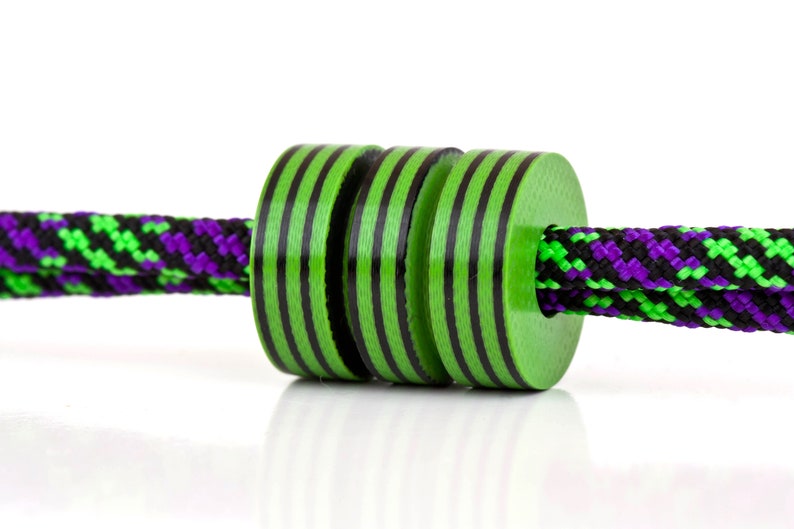 May include: Three green and black striped beads strung on a black and green rope with purple accents.