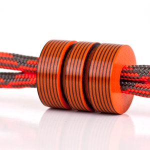 May include: Three orange and black striped beads are strung on a red and gray rope. The beads are cylindrical and have a glossy finish.