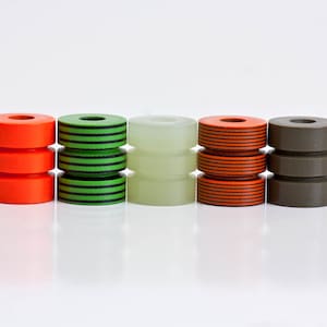 May include: Five stacked cylindrical beads in different colors and patterns. The beads are orange with black stripes, green with black stripes, white, orange with black stripes, and brown.