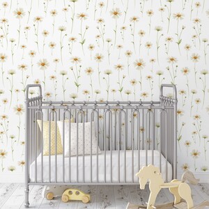 May include: A white crib with a silver metal frame and a white floral wallpaper with small yellow flowers. The crib has a white mattress and a white and yellow patterned pillow. A rocking horse and a toy car are on the floor in front of the crib.