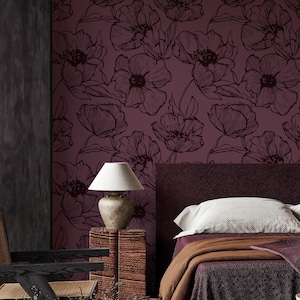 Può includere: Interno di camera da letto con carta da parati floreale bordeaux con contorni floreali scuri. Un letto con testiera bordeaux, cuscini bianchi e una coperta marrone è visibile. Una lampada con paralume beige è su un comodino in legno. Una sedia nera è in primo piano.