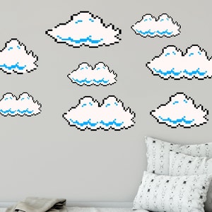 Pode incluir: Um conjunto de nove adesivos de parede de nuvens pixeladas em branco e azul. As nuvens estão dispostas em um padrão aleatório em uma parede cinza claro.