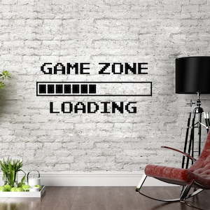 Może przedstawiać: Biała ceglana ściana z czarnym pikselowym napisem "GAME ZONE" z paskiem postępu i napisem "LOADING" poniżej. Na pierwszym planie znajduje się czerwony fotel bujany i czarna lampa.