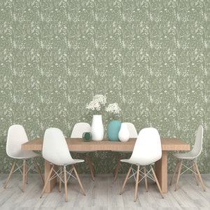 May include: A dining room table with six white chairs and a green floral wallpaper. There are three vases with white and blue flowers on the table.