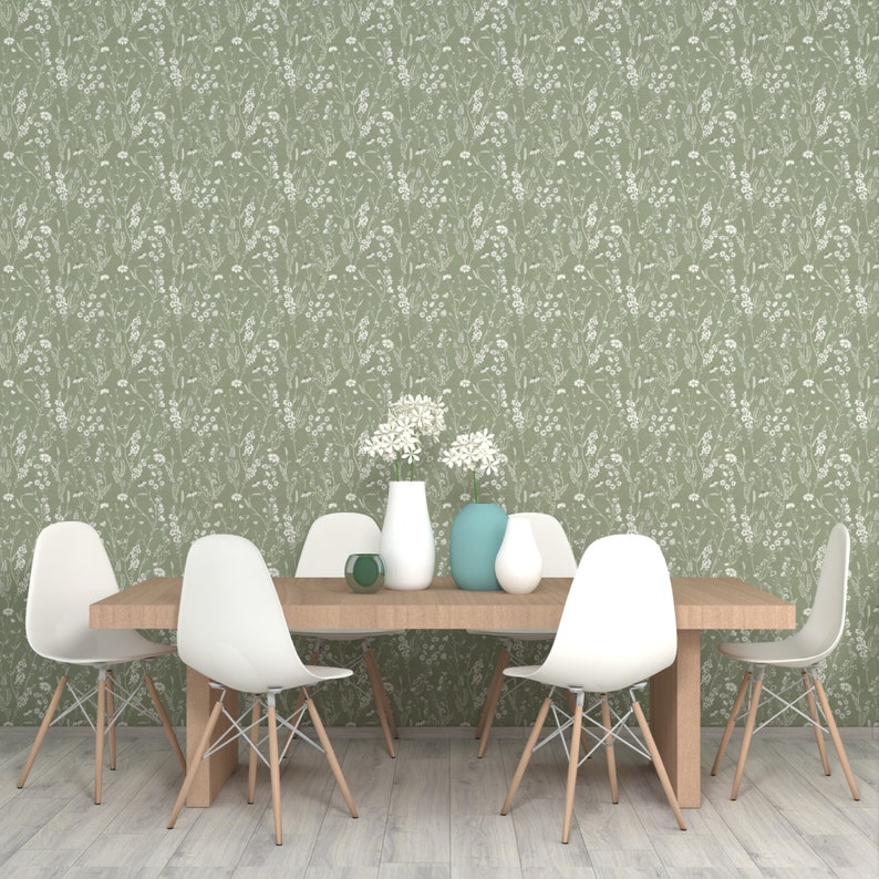 May include: A dining room table with six white chairs and a green floral wallpaper. There are three vases with white and blue flowers on the table.