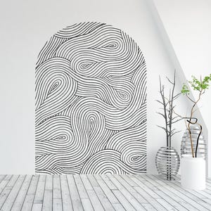 May include: A white wall with a black and white abstract design in the shape of an arch. The design is made up of wavy lines and circles. There are two plants in pots on the right side of the image.