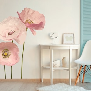 May include: Three pink poppy flower wall decals on a white wall with a white table and a white chair in the background.