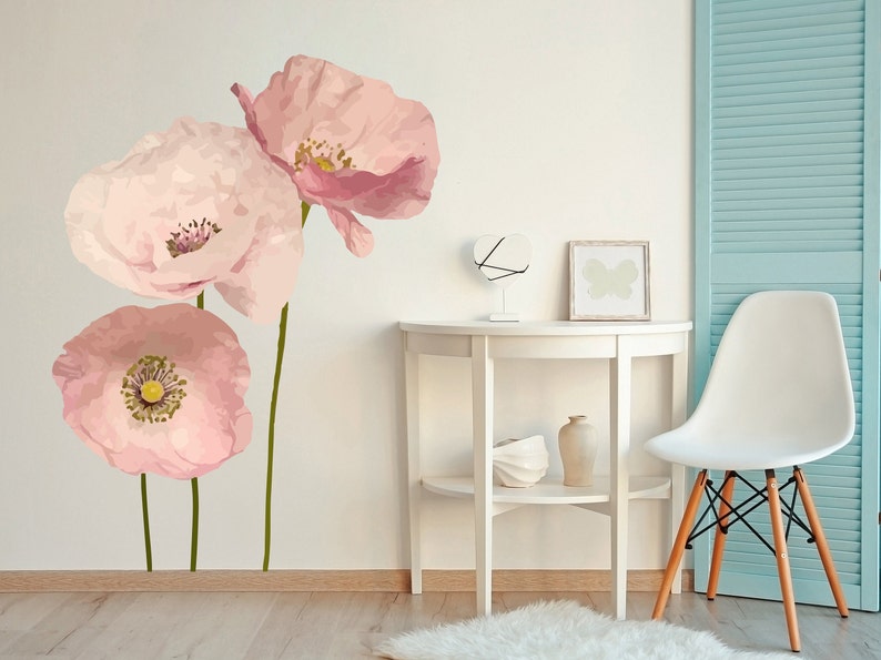 May include: Three pink poppy flower wall decals on a white wall with a white table and a white chair in the background.