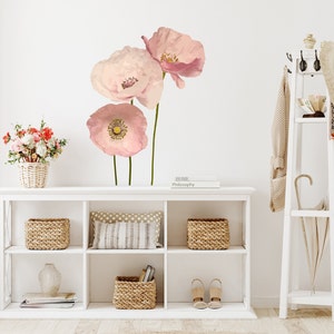 May include: A white shelf unit with three shelves, featuring a vase, baskets, and books. The wall behind the shelf has a pink floral decal with three large poppy flowers.