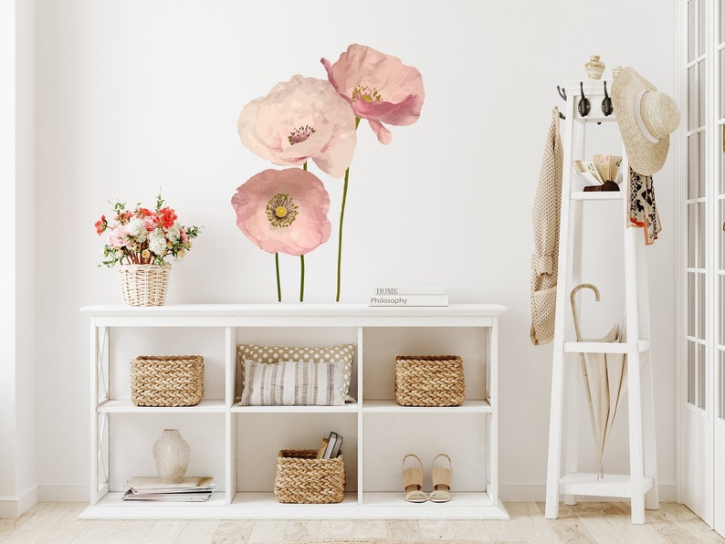 May include: A white shelf unit with three shelves, featuring a vase, baskets, and books. The wall behind the shelf has a pink floral decal with three large poppy flowers.