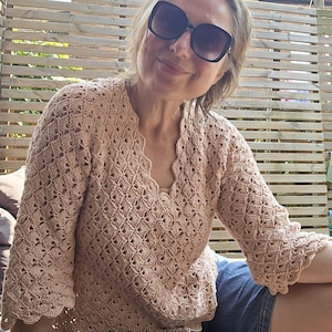 Può includere: Un top lavorato a uncinetto di colore marrone chiaro con scollo a V e maniche corte. Il top ha un delicato motivo a pizzo.