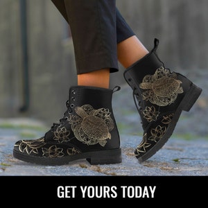 May include: Black leather lace-up boots with a gold outline of a sea turtle and floral designs. The boots are being worn by a person standing on a stone surface.