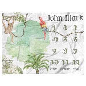 Könnte beinhalten: Eine weiße Baby-Meilenstein-Decke mit Dschungel-Motiv. Sie zeigt einen grünen Aquarellhintergrund mit einem Affen, einem Papagei und Palmen. Die Decke hat die Zahlen 1 bis 12 aufgedruckt, sowie die Wörter "Wochen", "Monate" und "Jahre". Der Name "John Mark" ist oben auf der Decke aufgedruckt.