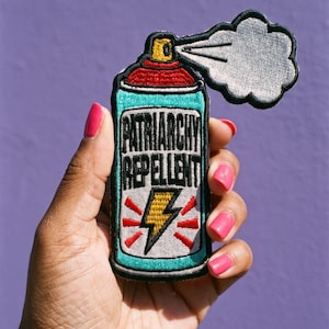 Puede incluir: Un parche bordado con forma de bote de spray con cuerpo color verde azulado, tapa roja y una nube de spray blanca. El texto "PATRIARCHY REPELLENT" está bordado en letras negras sobre un gráfico de rayo amarillo con detalles en rojo.