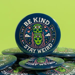 Puede incluir: Un conjunto de botones redondos azul marino con las palabras "BE KIND STAY WEIRD" que rodean un gráfico de un alienígena verde. Los botones están apilados sobre un fondo verde brillante, creando un diseño lúdico y llamativo.