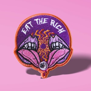 Può includere: Toppa ricamata viola e arancione con il testo "Eat the Rich" in bianco. La toppa presenta due labbra rosa con occhi e un design a spirale arancione e giallo al centro.
