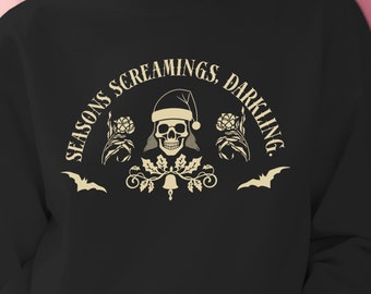 Op de afbeelding: Zwart sweatshirt met een wit grafisch ontwerp van een schedel met een kerstmanmuts en de tekst "Seasons Screamings, Darling".