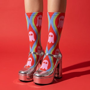 May include: Mid-calf socks featuring a red background with a repeating pattern of light pink ghosts and wavy blue and yellow lines, worn inside metallic silver platform Mary Jane shoes with a buckled strap and a thick block heel.