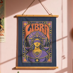Peut inclure: Une tenture murale rectangulaire présentant une illustration du signe du zodiaque Balance avec une figure aux yeux bandés tenant une balance, sur fond bleu foncé avec des accents orange et violets. L'œuvre est fixée sur un cadre en bois avec une corde.