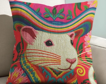 May include: Embroidered decorative pillow featuring a white rat wearing a colorful hat and collar against a red background. The pillow has a vibrant design with rainbow, pink, yellow, and green accents. The pillow is square and rests on a white sofa.
