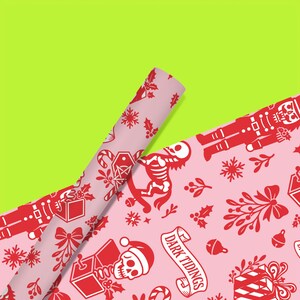 Premium satin finish wrapping paper featuring a repeating pastel goth pattern on a pink background. The design showcases a playful yet spooky aesthetic with high-contrast skeleton nutcrackers, skull jack-in-the-boxes, and rocking horse skeletons in soft pinks, and reds. The paper texture appears semi-glossy. Shown in three available sizes including sheets and rolls, specifically 29 inches wide, suitable for wrapping gifts for holidays, birthdays, or gothic themed occasions.